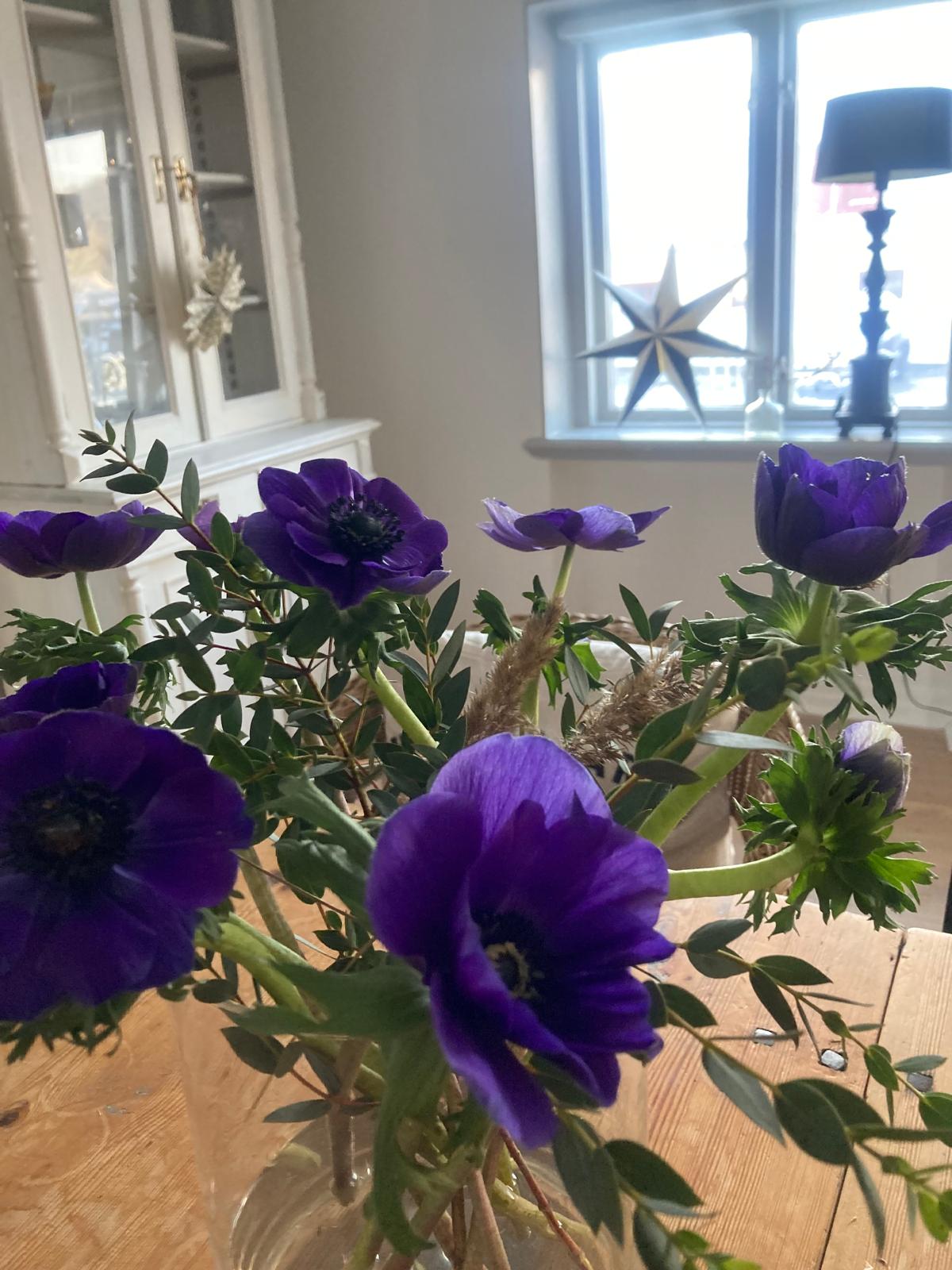 Lila anemoner i en smal glasvas på ett träbord