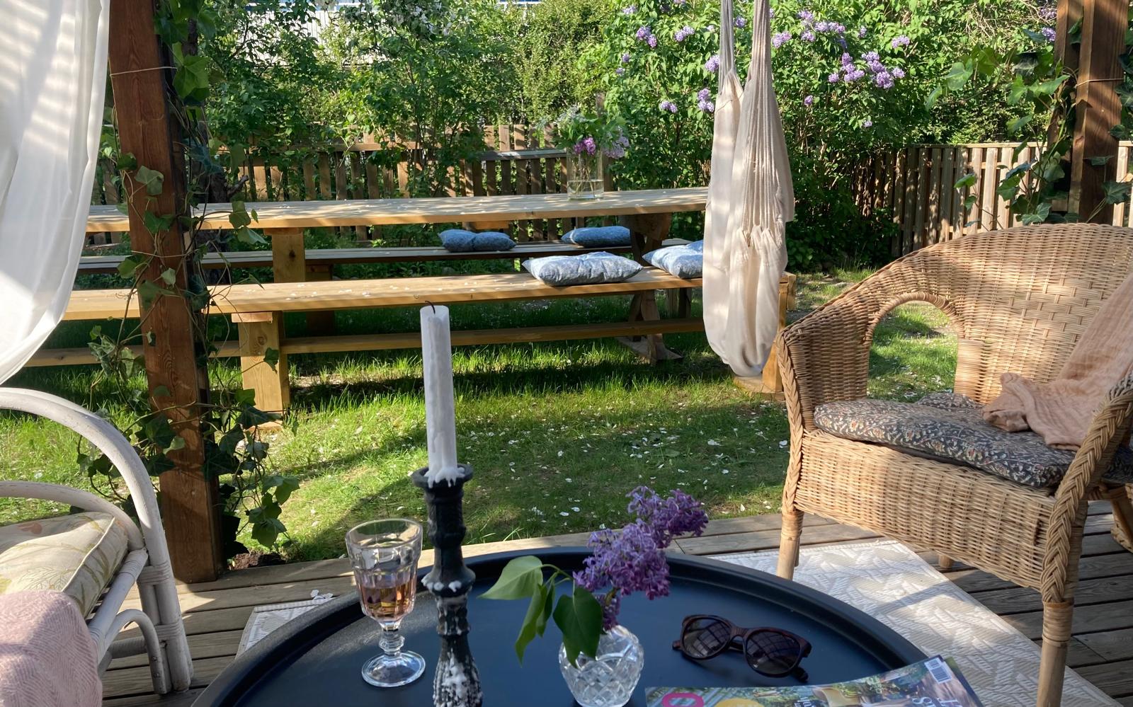 Mysig uteplats med dukat svart bord, rottingmöbler och blommande syrener